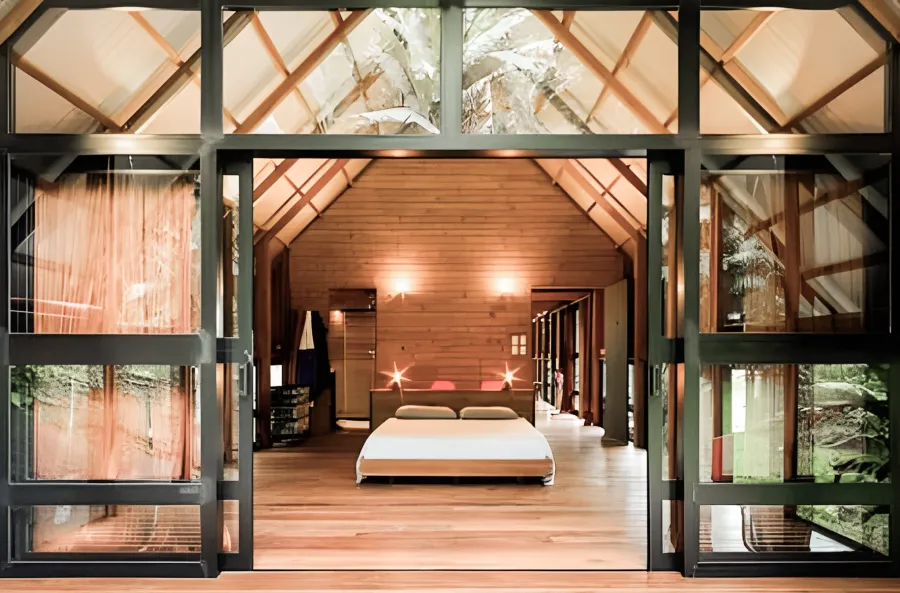 A bedroom open to the forest through walls of glass