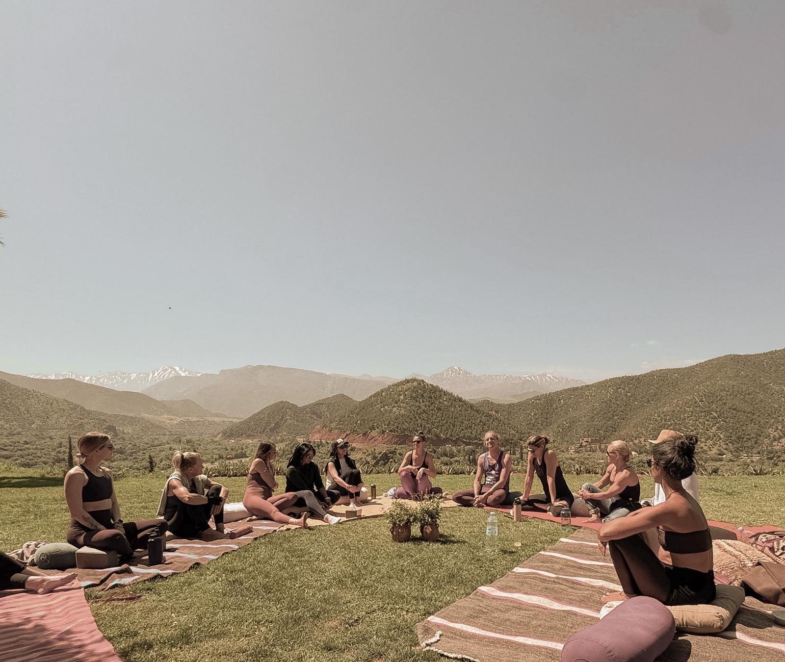 A circle gathered on the grass with the Atlas mountains behind
